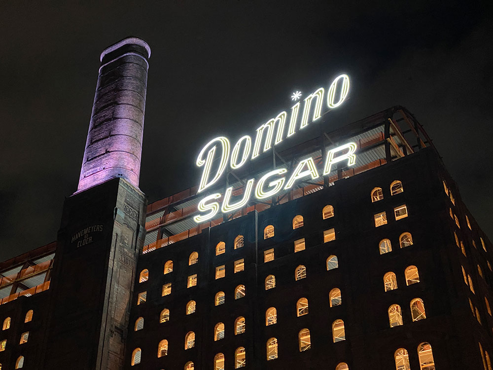Domino Sugar Factory sign on the williamsburg waterfront illuminated with the smokestake in purple
